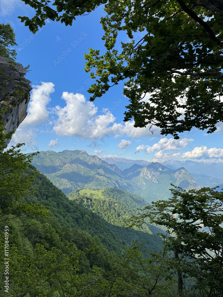 Beautiful mountain view of Swiss Alps next to Lugano lake and a small rock cliff on the left side and leaf tree branches on the right side, Lugano, Switzerland Beautiful mountain view of Swiss Alps next to Lugano lake and a small rock cliff on the left side and leaf tree branches on the right side, Lugano, Switzerland