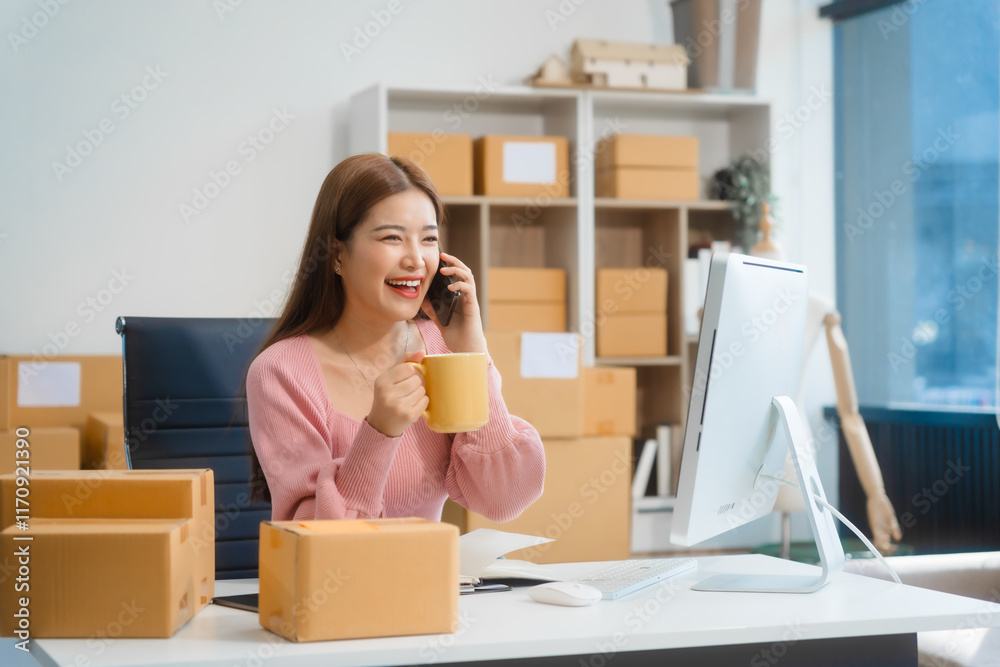 An Asian young woman sits in a room, working on a computer and making calls or video calls, managing her small business and online sales, surrounded by cardboard boxes ready for shipping. An Asian young woman sits in a room, working on a computer and making calls or video calls, managing her small business and online sales, surrounded by cardboard boxes ready for shipping.