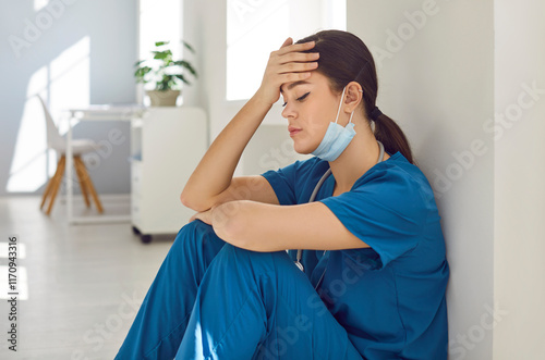 Tired and sad woman doctor, experiencing stress, burnout or the weight of a mistake, sits on the hospital floor. Nurse convey the human side of medicine, portraying the emotional toll.