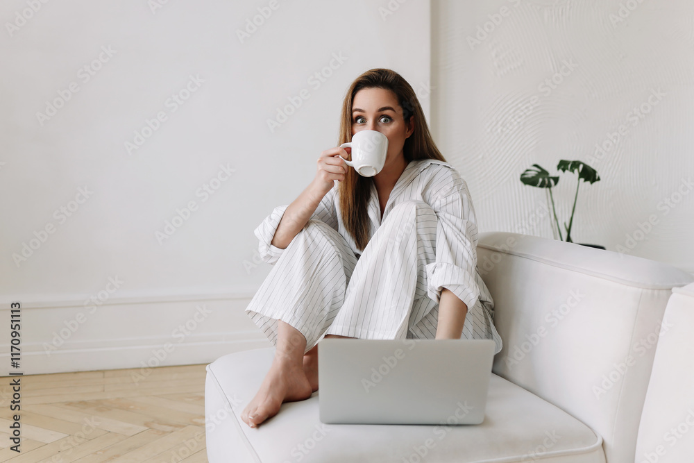 A woman in white pajamas is looking at a laptop, working and shopping online using technology while sitting on a sofa in a bright and comfortable apartment interior. Selective focus A woman in white pajamas is looking at a laptop, working and shopping online using technology while sitting on a sofa in a bright and comfortable apartment interior. Selective focus