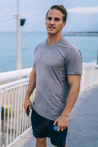 Half length portrait of caucasian man jogger standing near quay enjoying morning workout keeping physical strength, young handsome male in activewear looking at camera keeping healthy lifestyle photo