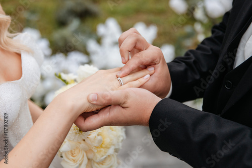 Close-up photo of the groom putting on his wife's wedding rings and holding her hand, showing his love and loyalty