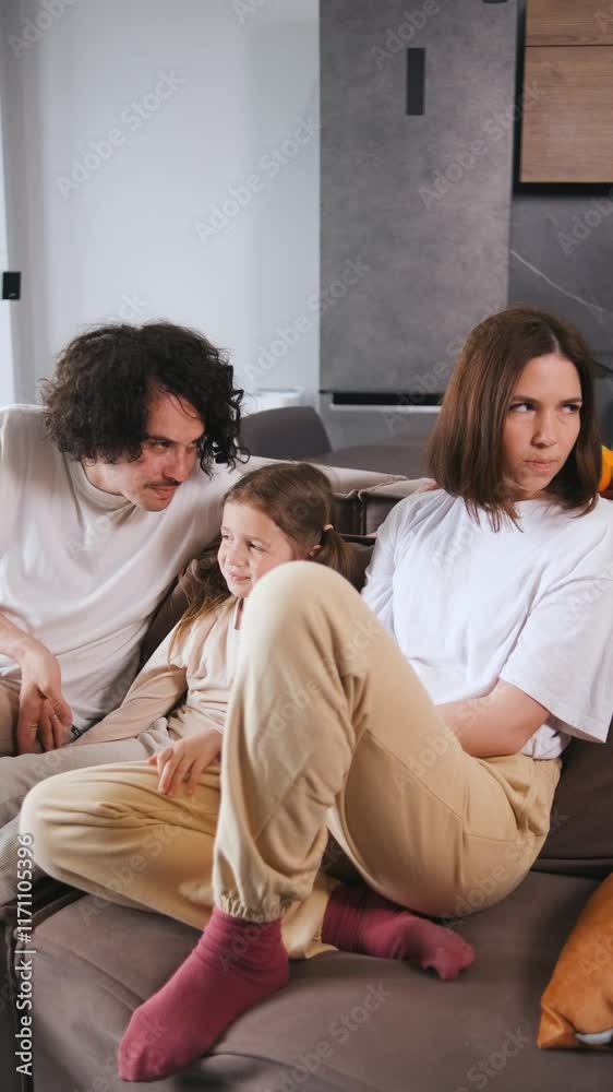Vertical video Mom is sitting on the couch, feeling sad and upset, while dad and their young daughter try to cheer her up with smiles and laughter Vertical video Mom is sitting on the couch, feeling sad and upset, while dad and their young daughter try to cheer her up with smiles and laughter
