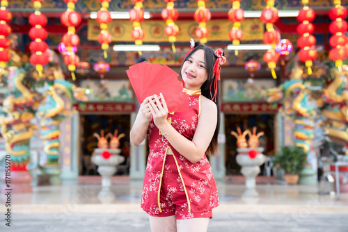 Portrait smiles Asian young woman wearing red cheongsam dress holding red envelopes decoration for Chinese new year festival celebrate culture of china at Chinese shrine Public places in Thailand