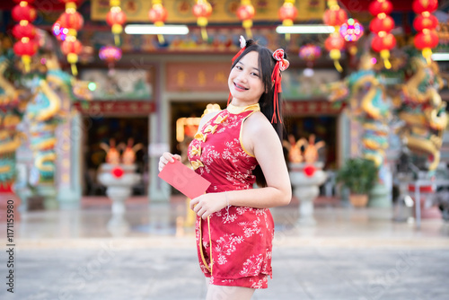 Portrait smiles Asian young woman wearing red cheongsam dress holding red envelopes decoration for Chinese new year festival celebrate culture of china at Chinese shrine Public places in Thailand