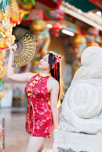 Obraz na płótnie Portrait beautiful cute smiles Asian young woman wearing red traditional Chinese cheongsam decoration and holding a Chinese Fanning for Chinese New Year Festival at Chinese shrine in Thailand w salonie
