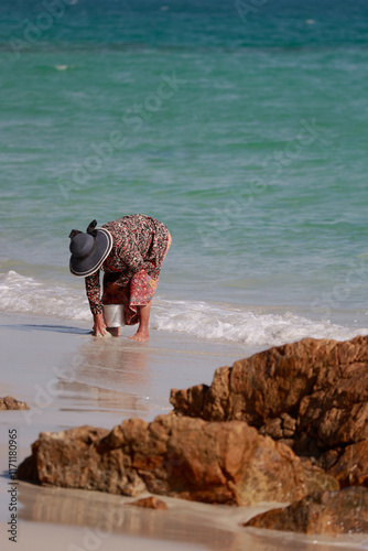 an elderly woman collects shellfish on the coast on Koh Samet