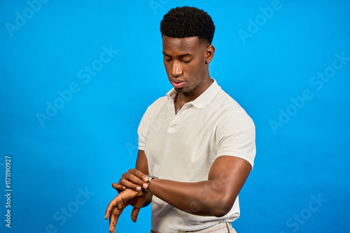 Young man checking time on wristwatch on blue background