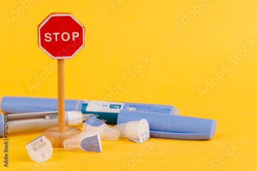 Wooden stop sign and glucose control medication pen with semaglutide on yellow background photo