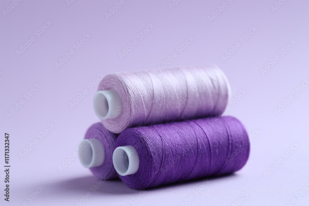 Spools of colorful sewing threads on lilac background, closeup Spools of colorful sewing threads on lilac background, closeup