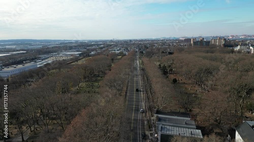 A panoramic view of  Jersey city a New york city  across a body of water.  In the foreground, a highway and industrial area are visible. The sky is partly cloudy, offering a balanced contrast.