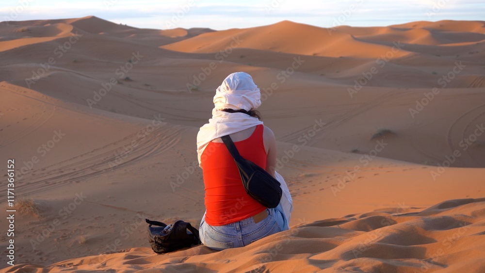 tourist girl with turban looking the beauty of the sand dunes of the Sahara Africa desert in Morocco in Merzouga, meditation and love for nature, relax and inspirazione during a travel Journey