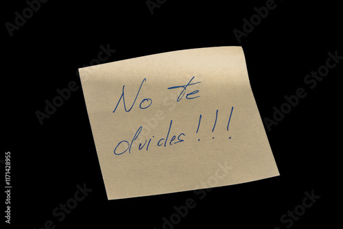 Yellow adhesive paper, similar to a Post-it note, on a black background with the words “No te olvides” in Spanish handwritten in blue ink.