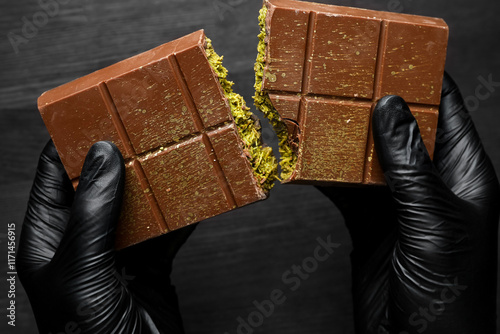 Photography Woman breaking Dubai chocolate bar with pistachio and knafeh at dark table, clos