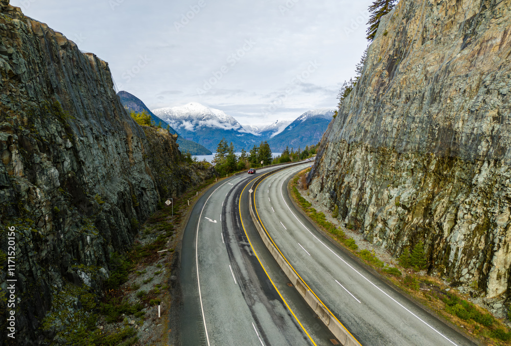 Fototapeta premium Peaceful Highway Along Rocky Cliffs with Snowy Mountain Views in British Columbia