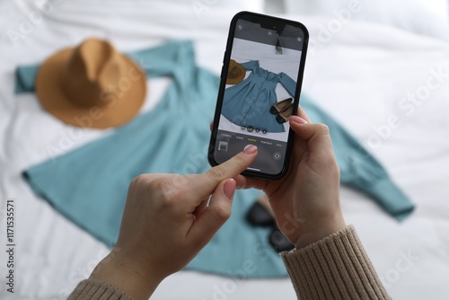 Woman with smartphone taking photo of her used clothes indoors, selective focus photo