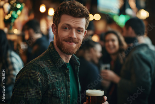 A man celebrates Saint Patrick's Day in a bustling pub, sporting a beard and a green shirt. He joyfully holds a beer as he mingles with others in the festive setting.