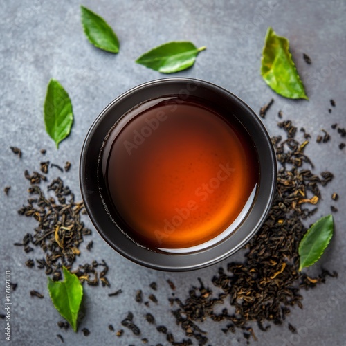 Warm cup of black tea surrounded by loose leaves and fresh herbs on a texture...