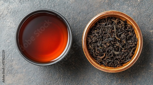 Black tea served in a cup with fresh tea leaves and loose tea on a dark surface