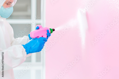 Person painting a wall with a spray gun in a bright room with pink walls photo