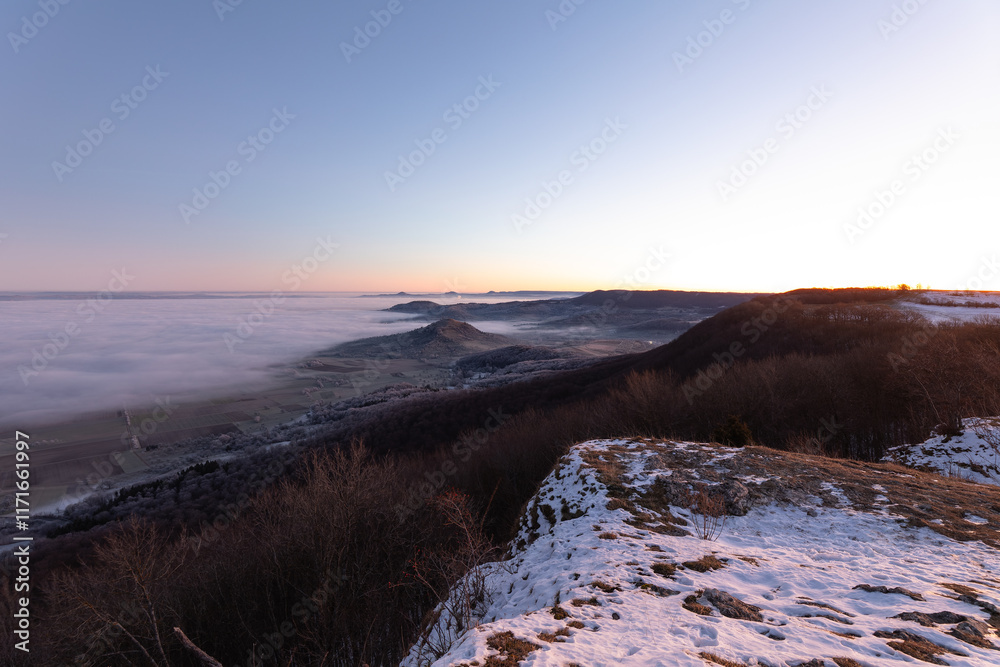 Obraz premium Blick vom Breitenstein, Ochsenwang, Schwäbische Alb auf die drei Kaiserberge - Hohenstaufen, Stuifen und Rechberg. Im Vordergrund die Limburg bei Weilheim Teck im Winter zum Sonnenaufgang mit Nebel.