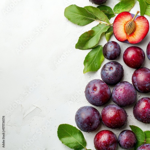 Fresh plums arranged with leaves on a light background showcasing vibrant col...