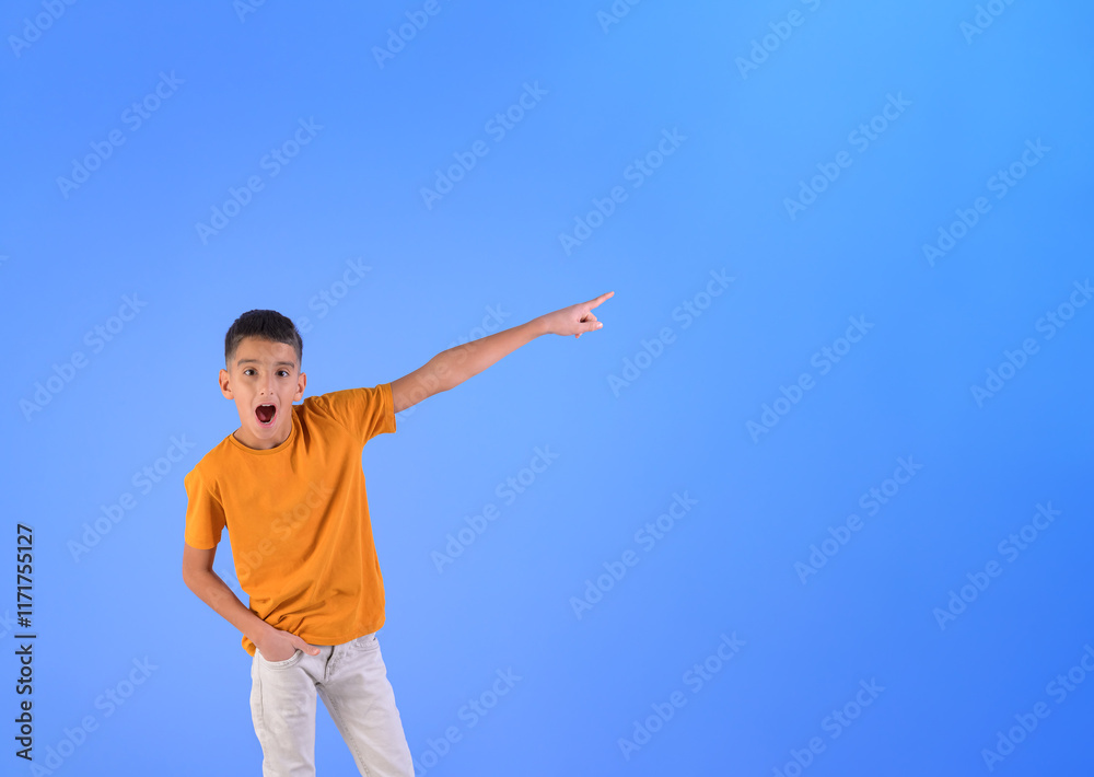 Portrait of surprised boy with mouth open pointing at blank space while standing on blue background Portrait of surprised boy with mouth open pointing at blank space while standing on blue background