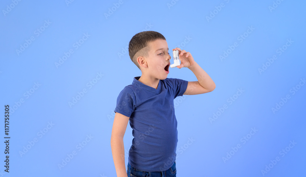 Portrait of adorable boy inhaling through asthma pump while standing against isolated blue background Portrait of adorable boy inhaling through asthma pump while standing against isolated blue background