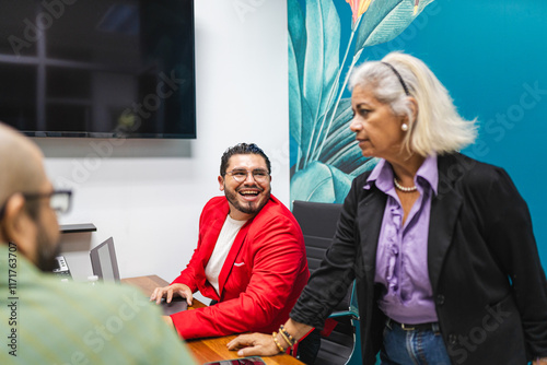 A smiling man in a red suit interacts with his colleagues during a meeting in a modern office. photo