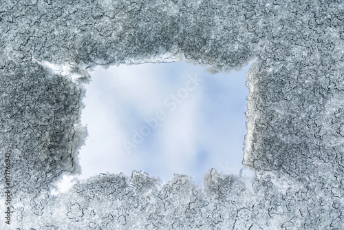 Ice-Covered Surface with Clear Patch. Close-up of an icy surface with a cleared patch revealing a pale blue sky, showcasing intricate frost patterns and textures. Copy space. photo