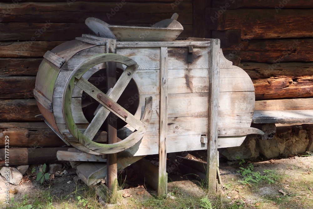 An old winnowing machine standing against the wall of a wooden house An old winnowing machine standing against the wall of a wooden house