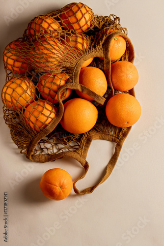 Ripe oranges in a reusable mesh shopping bag on a light surface. Sustainable lifestyle and zero waste concept.