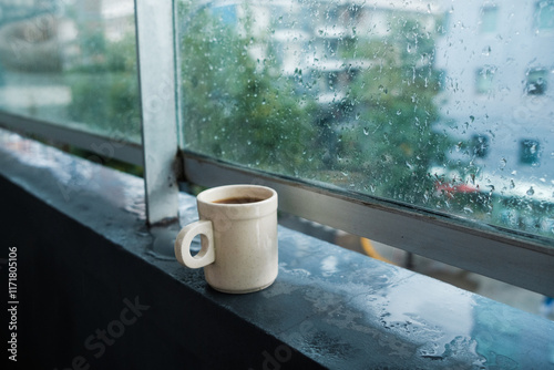 A warm cup of fresh coffee is gently resting on a window sill while a soothing rain falls outside on a cozy, rainy day