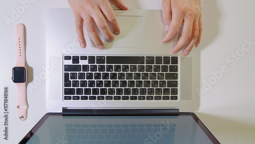 Freelancer working remotely from home or office, using laptop with cyrillic keyboard and smartwatch on white desk in top view