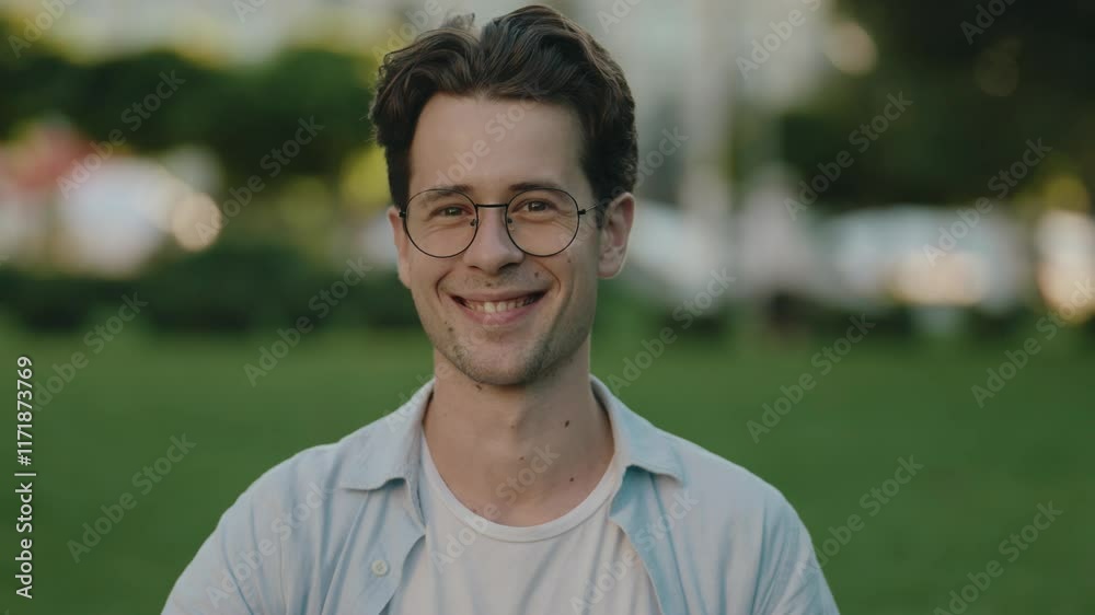 Portrait of a happy young man smiling at the camera in the park. He wears glasses and smiles sincerely. Slow motion. Portrait of a happy young man smiling at the camera in the park. He wears glasses and smiles sincerely. Slow motion.
