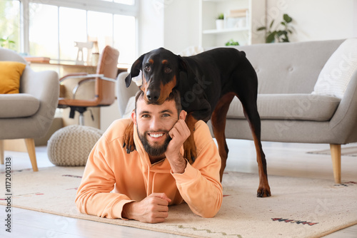 Cuadro en lienzo Young man with Dobermann dog lying on carpet at home