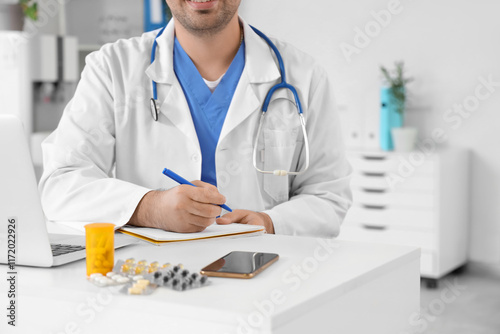 Male doctor writing in note...