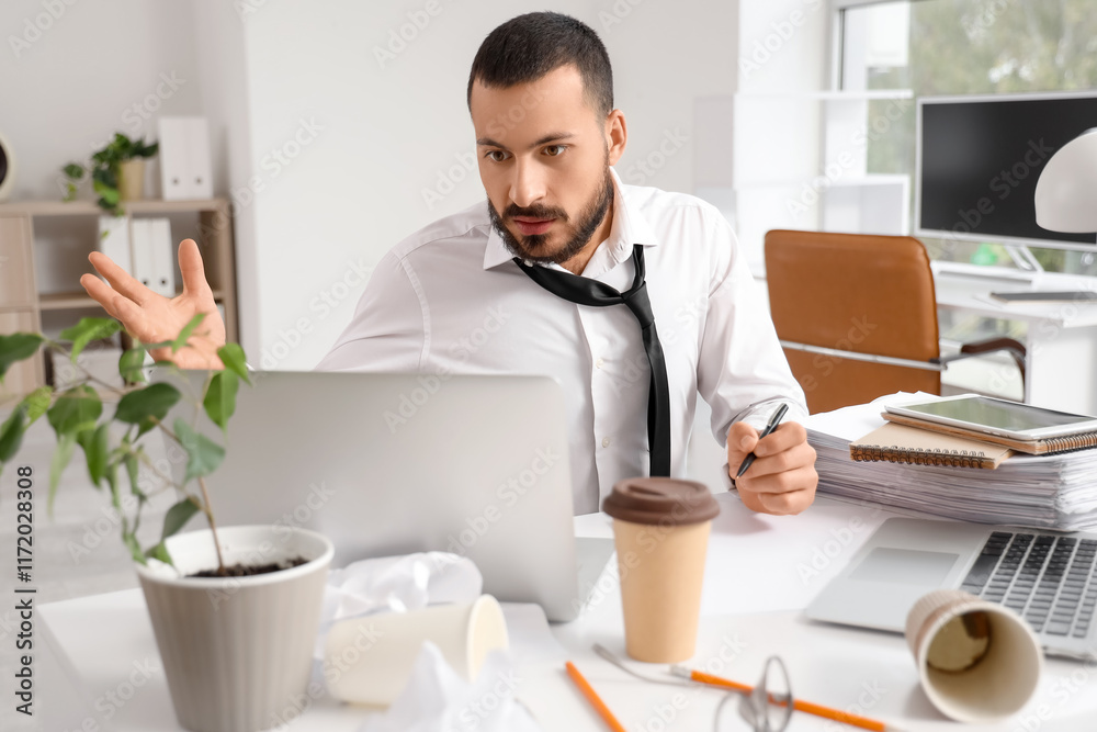 Stressed businessman working with laptops at table in office