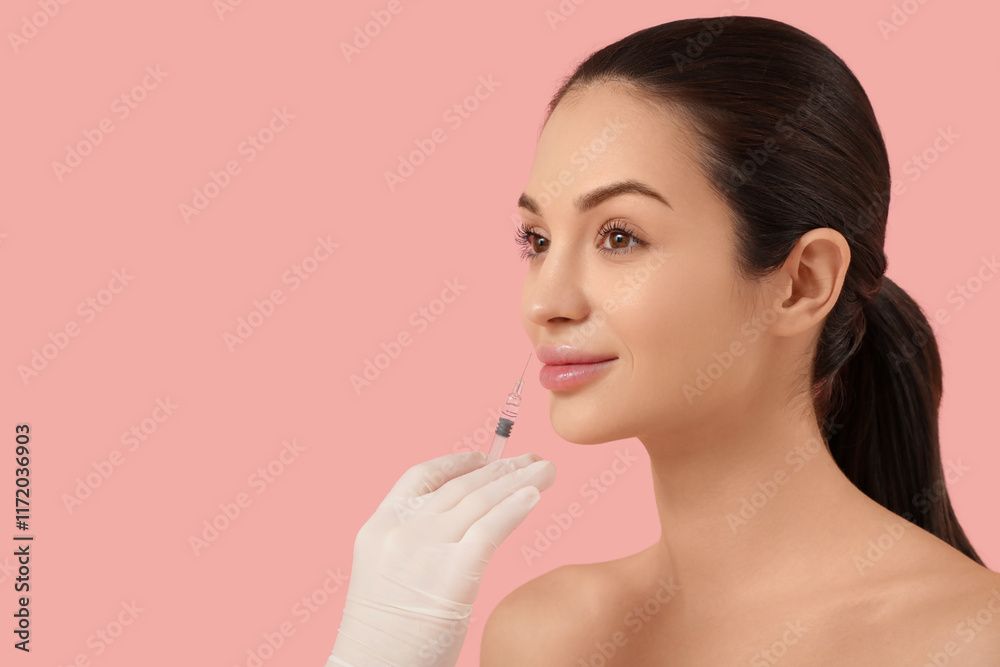 Beautiful young happy woman receiving lips injection on pink background