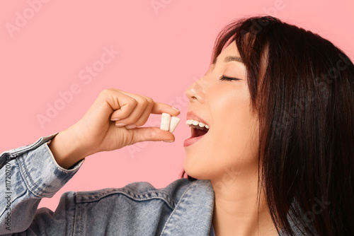 Fotografie Pretty young Asian woman with open mouth holding chewing gums on pink background