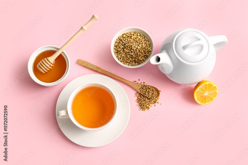 Fototapeta premium Cup and teapot of hot buckwheat tea with lemon and bowl of honey on pink background