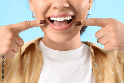 Smiling young woman with healthy teeth on blue background, closeup