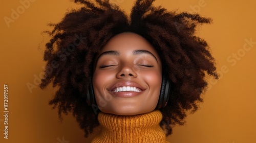 Joyful young woman with natural curls wearing headphones and smiling serenely against a vibrant orange background, embodying music and happiness with style.