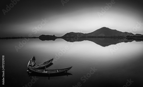 In the stillness of a black-and-white world, a few wooden boats are moored on the shore of a placid lake photo