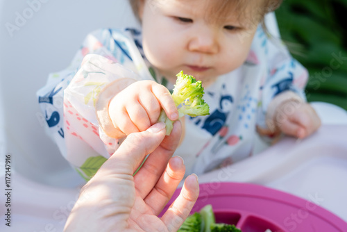 Little baby grabbing food from mother's hand. Baby touching food. Introducing solids to baby concept. Baby-led weaning concept
