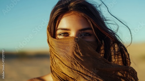A beautiful woman with her face covered by a scarf, standing gracefully in the vast, golden desert under the clear blue sky, creating a sense of mystery and elegance.