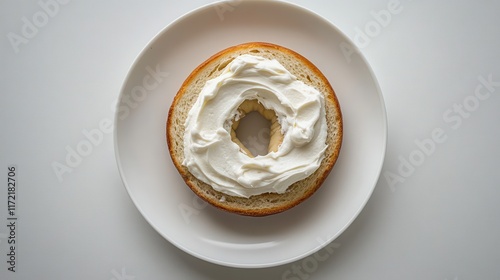 Cream cheese spread on a bagel half, on a white plate. Perfect for breakfast menus, food blogs, or recipes showcasing bagels and cream cheese.