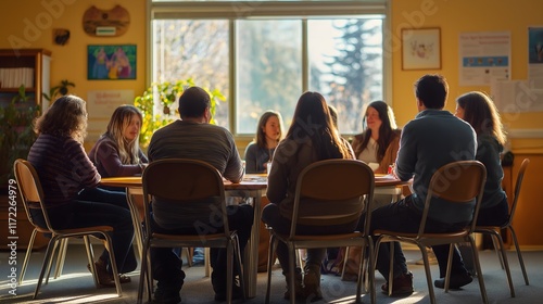 Group therapy session for seniors sitting at a round table with natural light coming in through a large window.