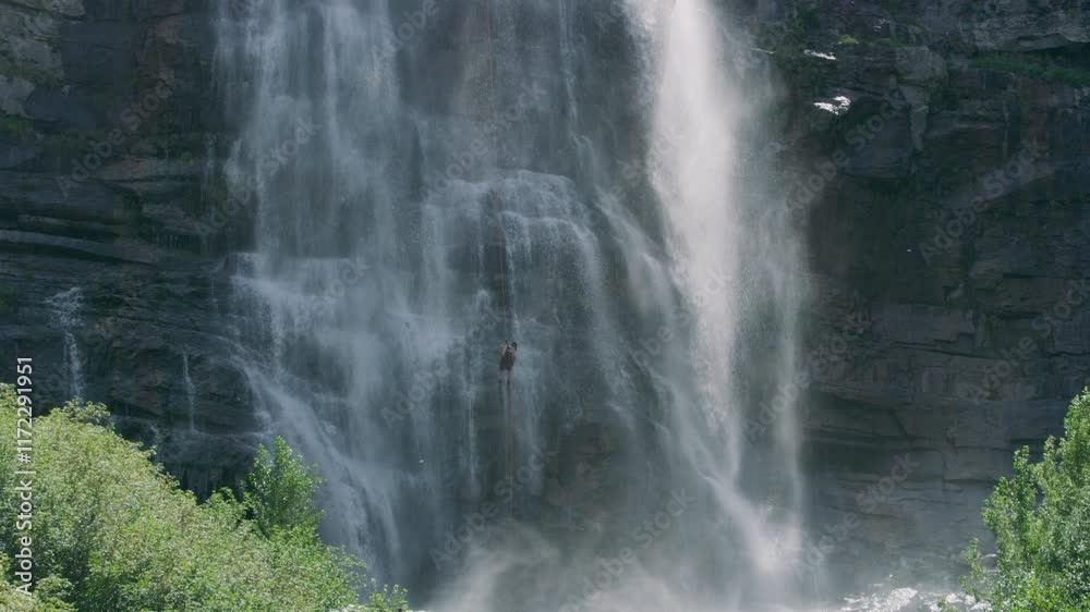 Wide shot of person rappelling down cliffside of large waterfall Wide shot of person rappelling down cliffside of large waterfall