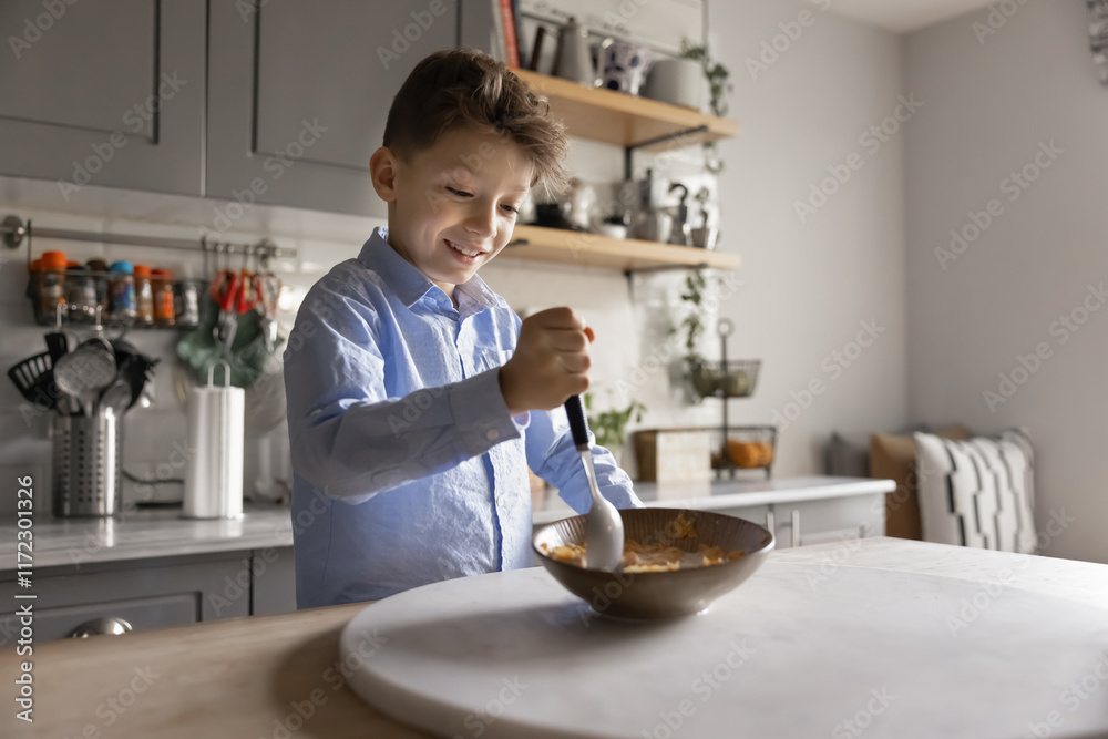 Happy positive boy kid stirring flakes and milk in bowl, eating at home, having breakfast in kitchen, holding spoon, enjoying tasty delicious food, preparing healthy cereal by himself, smiling Happy positive boy kid stirring flakes and milk in bowl, eating at home, having breakfast in kitchen, holding spoon, enjoying tasty delicious food, preparing healthy cereal by himself, smiling